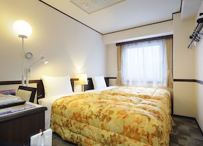 A hotel room with two beds, a desk with a lamp, a clock, and a window with curtains.