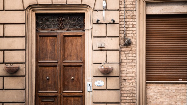 A double wooden door with a metal decorative grille, a wall-mounted light fixture, and a window with a brown shutter. - B&B Patrizio (San Benedetto del Tronto)