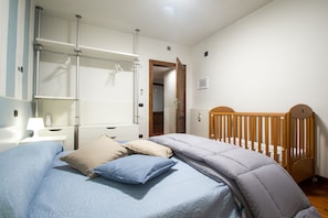 Ein Schlafzimmer mit einem Bett, einem Holckrippenbett, einem Nachttisch und einem an der Wand befestigten Regal.