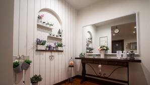A bathroom with a wooden floor, white walls with vertical lines, a large mirror, and shelves with plants and toiletries. - B&B Patrizio (San Benedetto del Tronto)