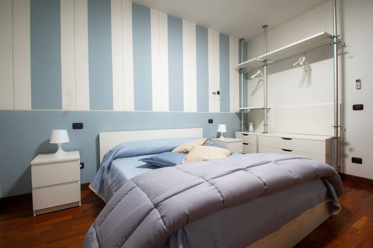 Ein Schlafzimmer mit einem Bett, Nachttischen, einer Kommode, einem Spiegel und einer gestreiften Wand.