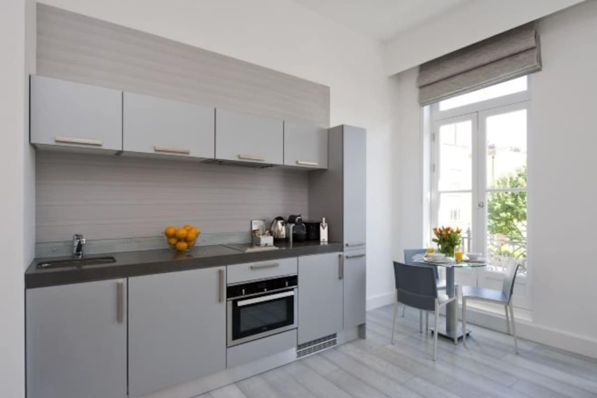 A modern kitchen with grey cabinets, a built-in oven, and a dining area with a table and chairs.