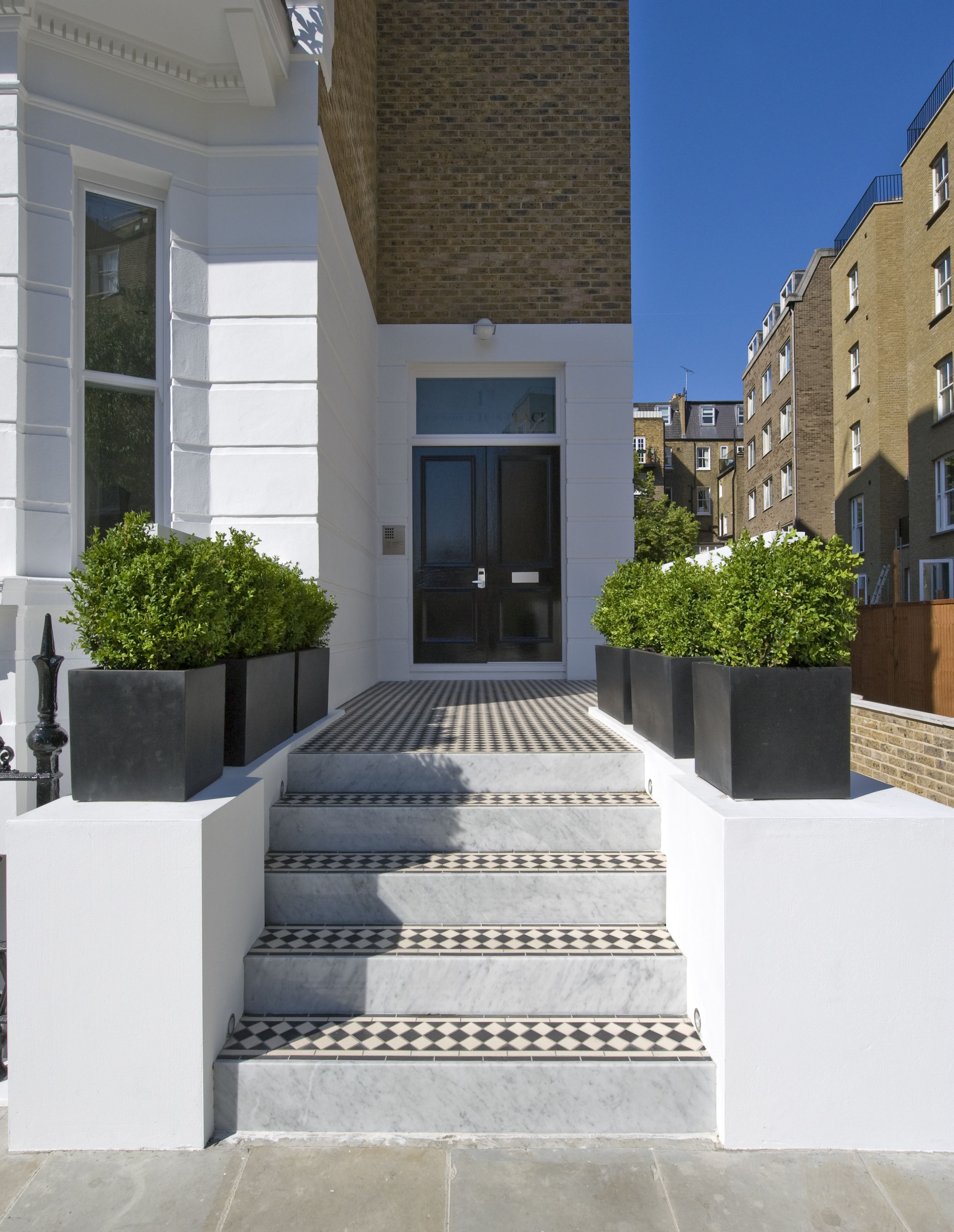 A modern building with a white facade, a black door, and a tiled entrance.