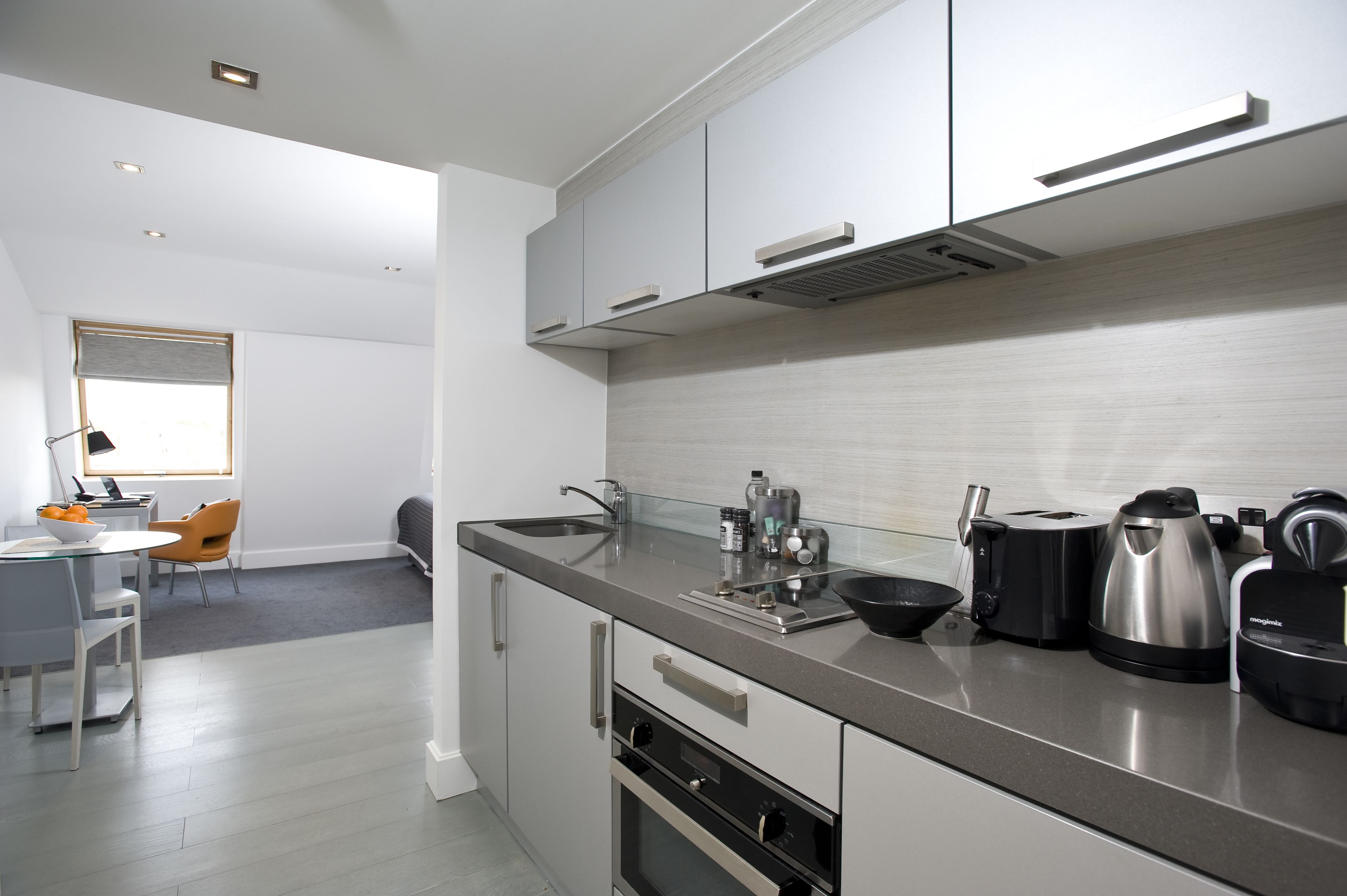 A modern kitchen with stainless steel appliances, a dining area with a table and chairs, and a window with blinds.
