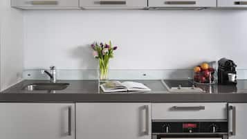A modern kitchen with a stainless steel sink, a vase of flowers, a bowl of fruit, and a coffee machine.