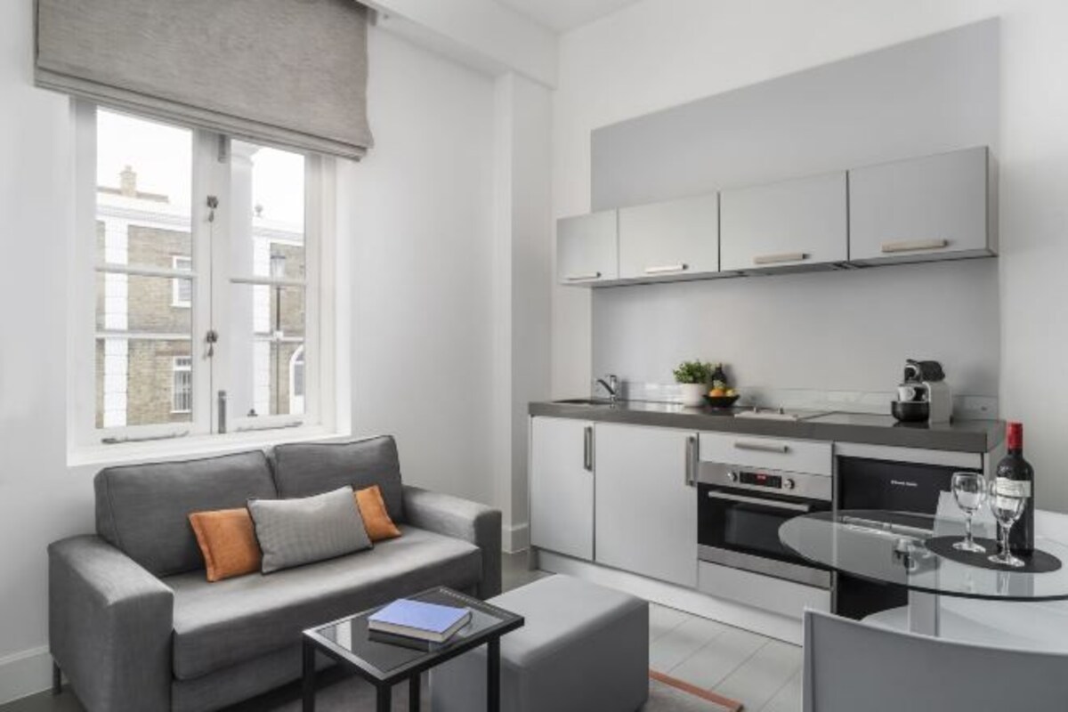 A modern kitchen with white cabinets, a built-in oven, and a dining area with a glass table.