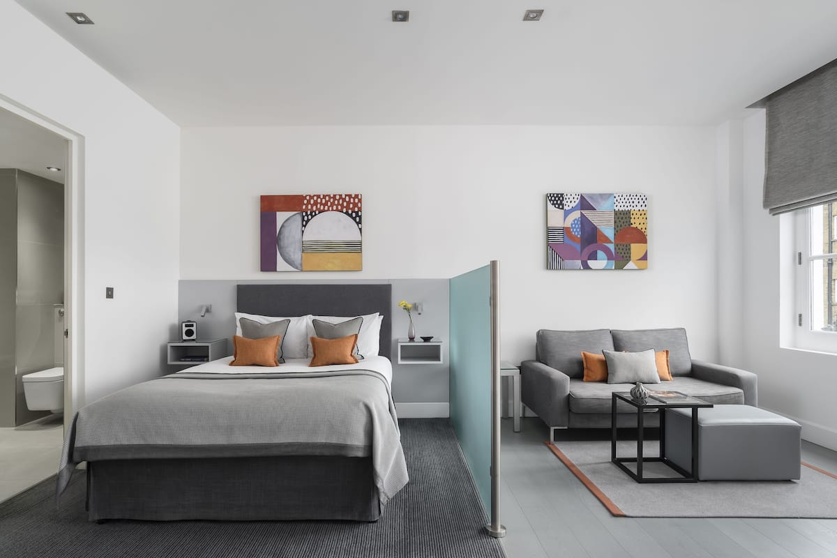 A modern bedroom with a large bed, a grey sofa, and two abstract paintings on the wall.