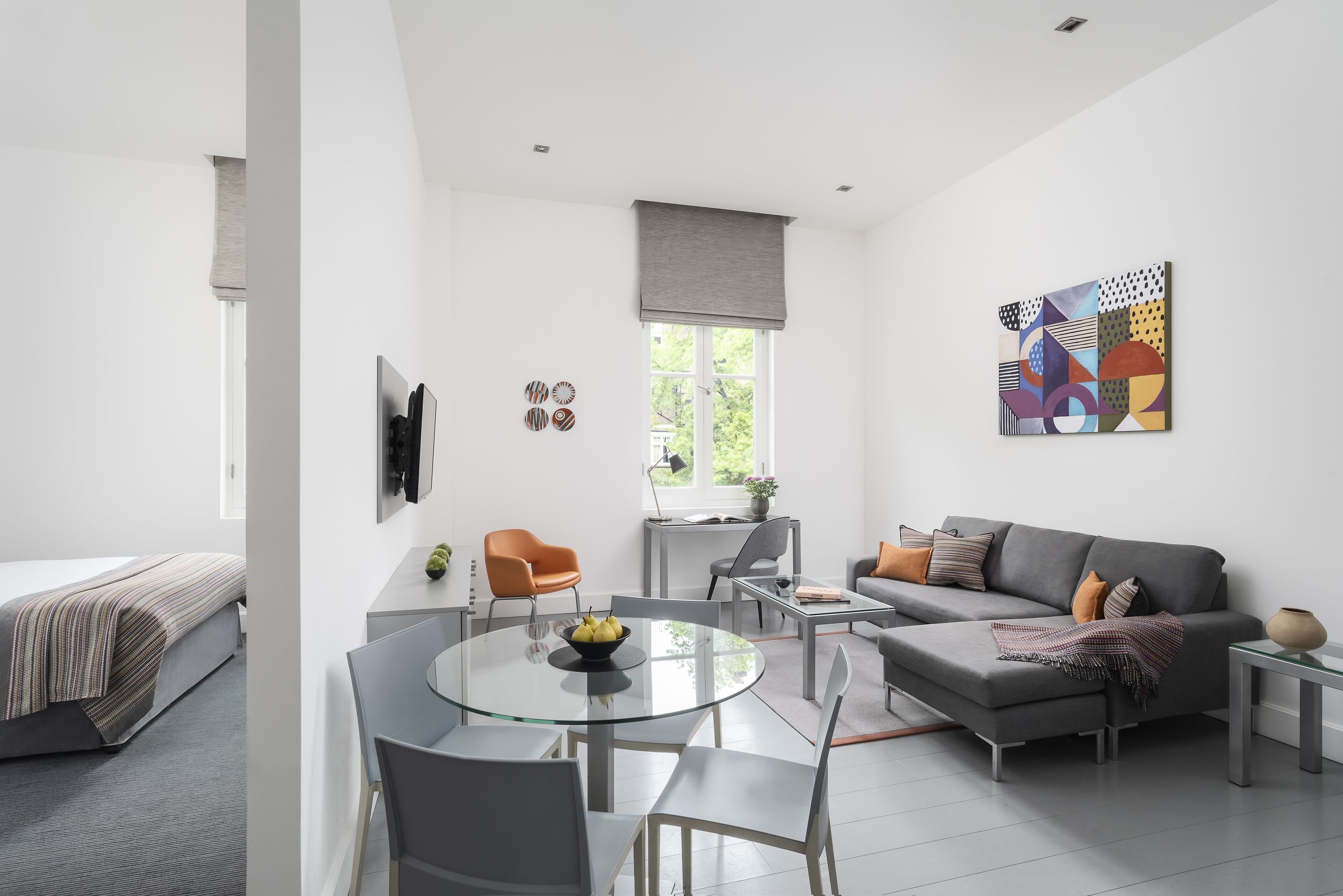 Une pièce moderne et bien éclairée, comprenant un lit, un canapé, une table à manger avec des chaises et un téléviseur fixé au mur.