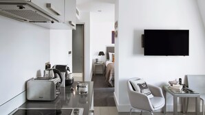 A modern hotel room with a kitchenette, a flat-screen TV, a bed with a headboard, a bedside table, and a chair. - Templeton Place by Supercity Aparthotels (London)