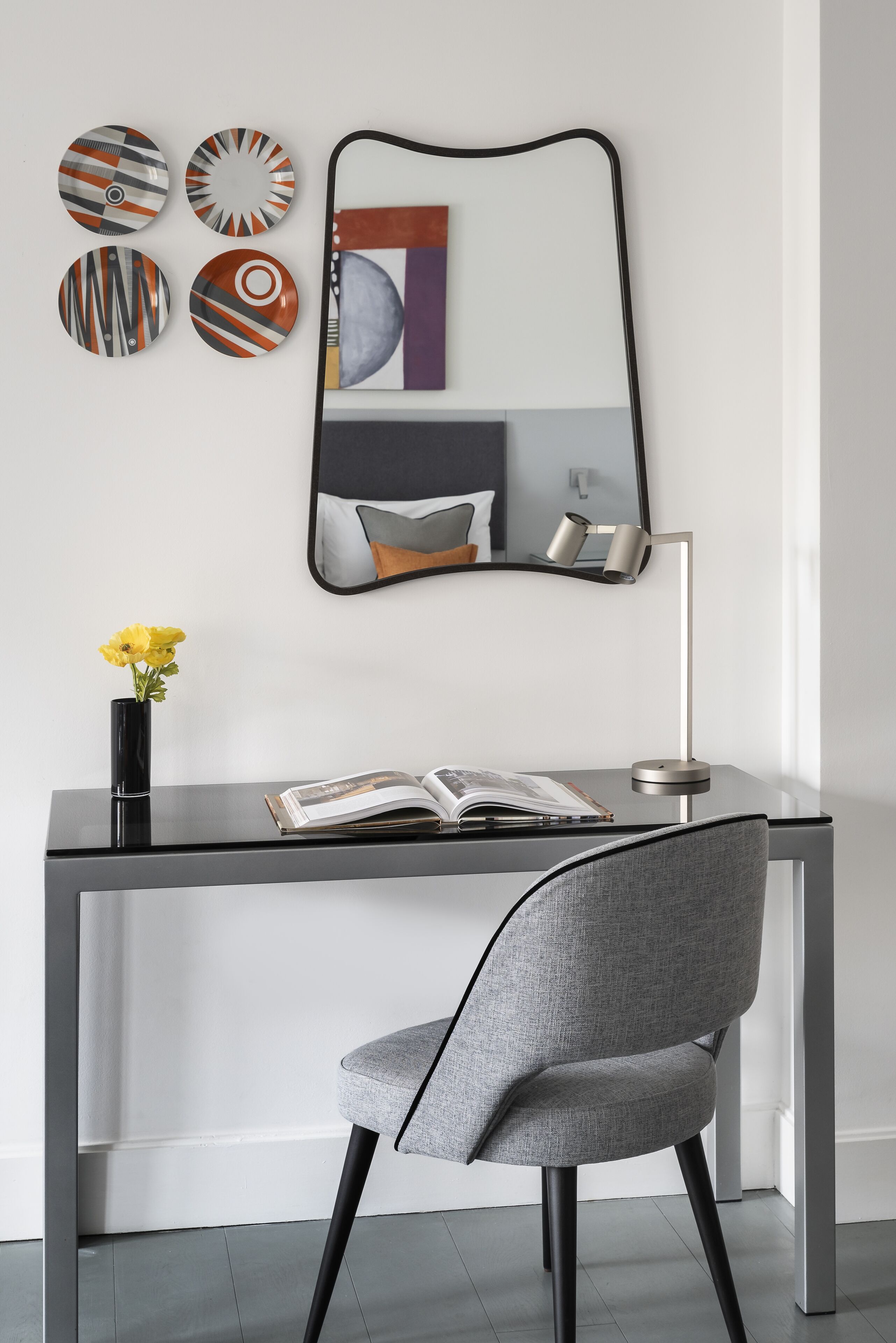 Un escritorio moderno con una silla, un espejo y platos decorativos en la pared.