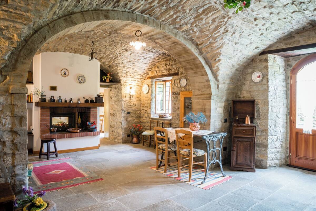 Un intérieur rustique aux murs de pierre, agrémenté d’une cheminée, de meubles en bois et d’un coin repas.