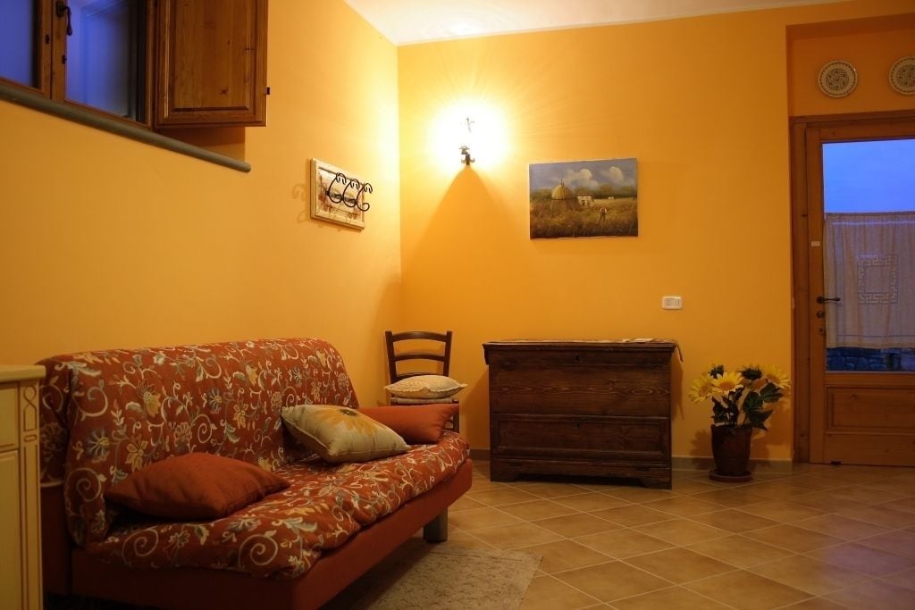 Uma sala de estar com um sofá, um armário de madeira, uma poltrona, uma luminária na parede e uma porta.