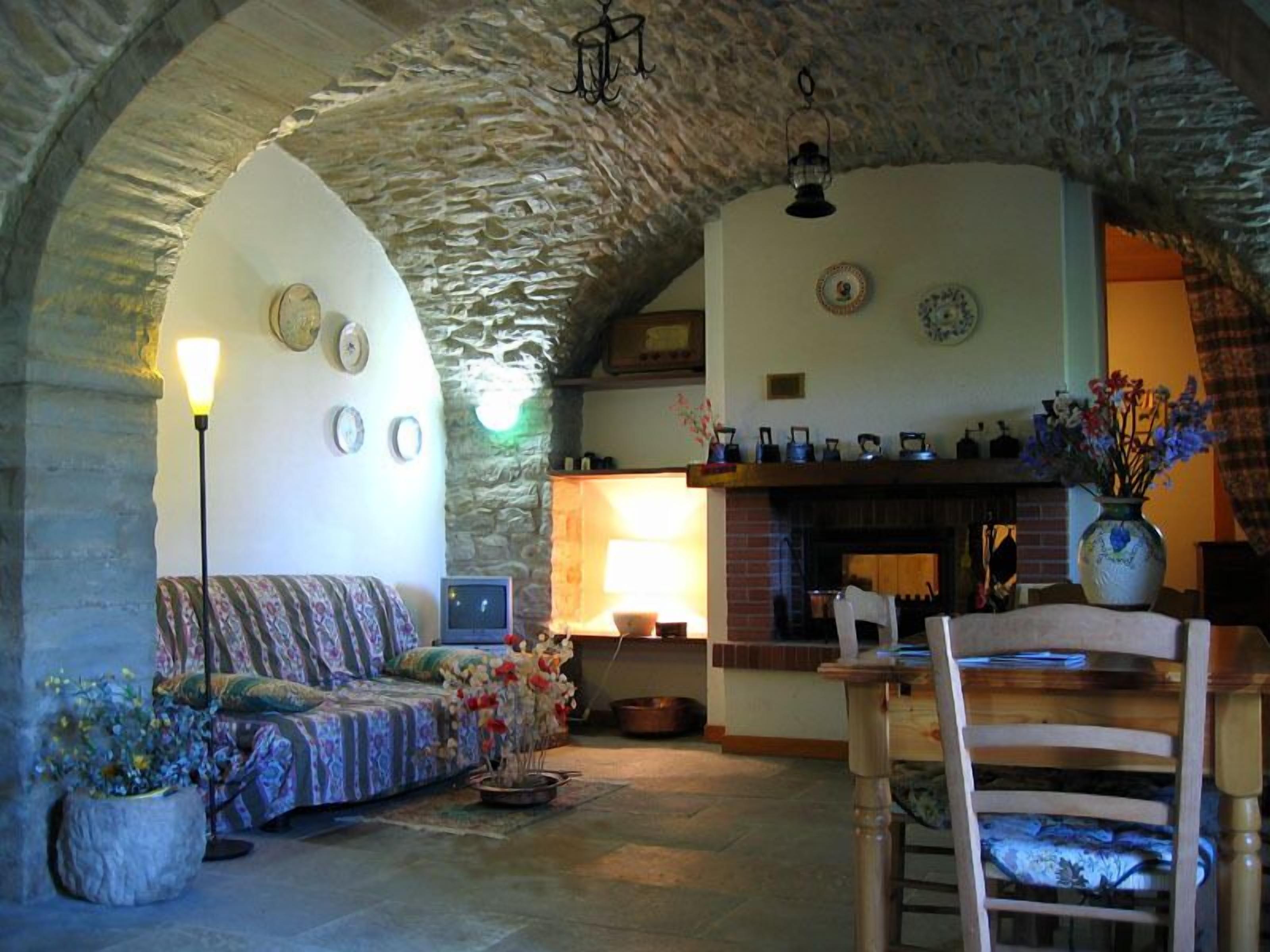 A cozy living room with a stone archway, a sofa, a wooden chair, a fireplace, and a variety of decorative items.