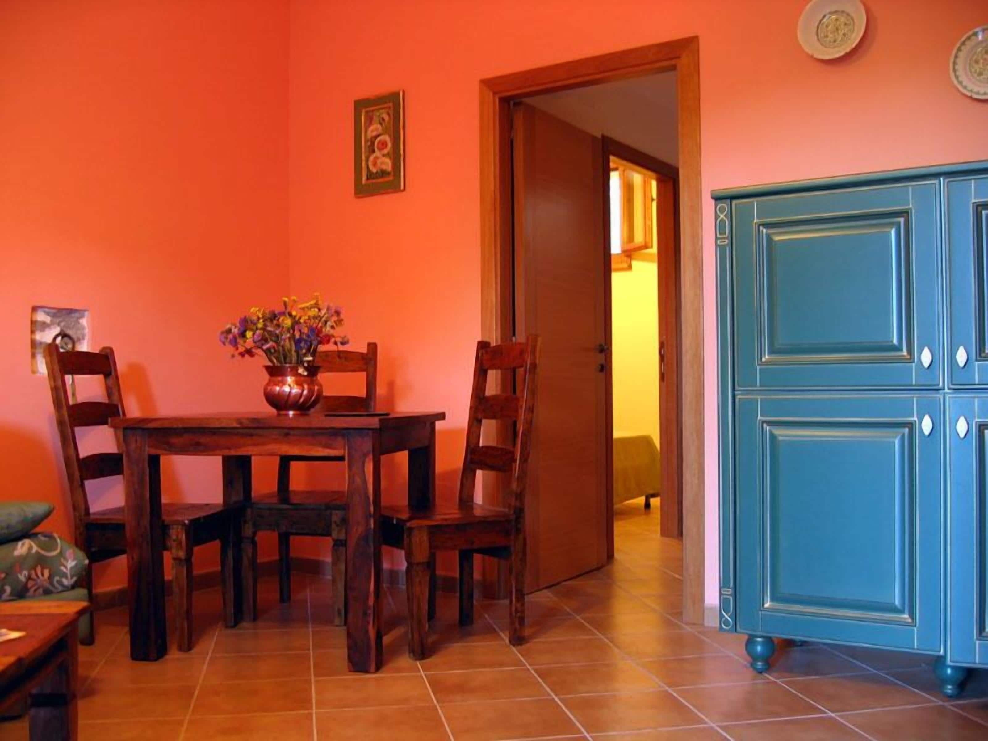 A dining area with a wooden table and chairs, a vase with flowers, and a blue cabinet.