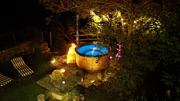 Un jacuzzi rodeado de asientos de piedra, una escalera de madera y una mesa de piedra con velas.