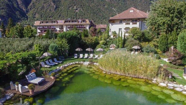 A resort with a clear pool, lounge chairs, and a mountainous backdrop. - Hotel Rössl (Parcines)