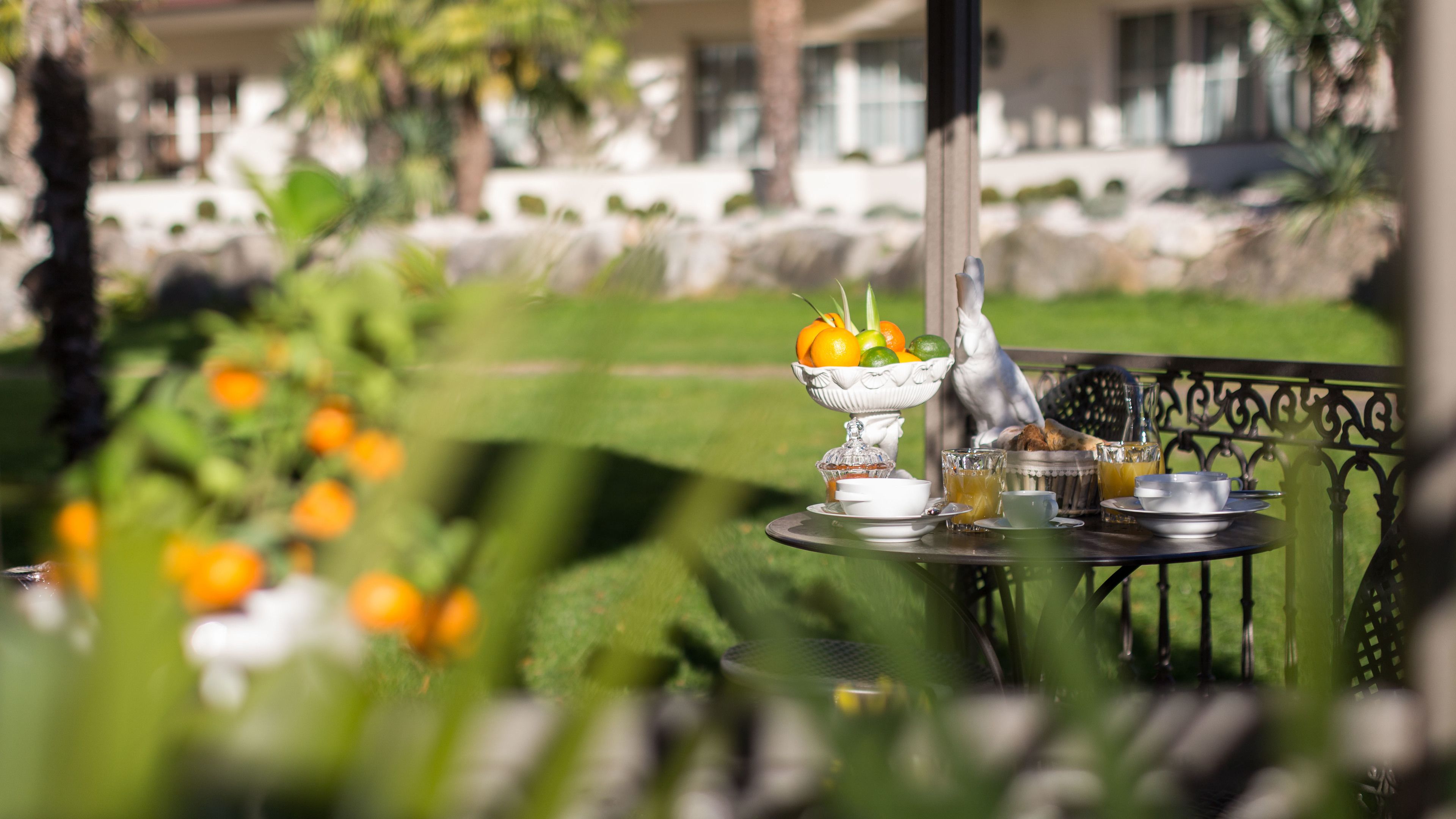 A table set outdoors with a fruit bowl, cups, and a bottle.