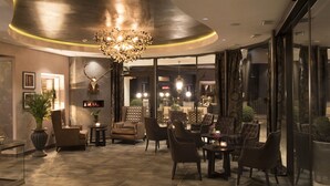 A modern interior with a fireplace, leather chairs, and a chandelier. - Hotel Rössl (Parcines)