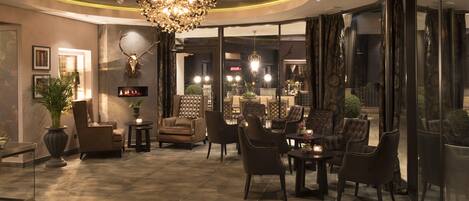 A modern interior with a fireplace, leather chairs, and a chandelier.