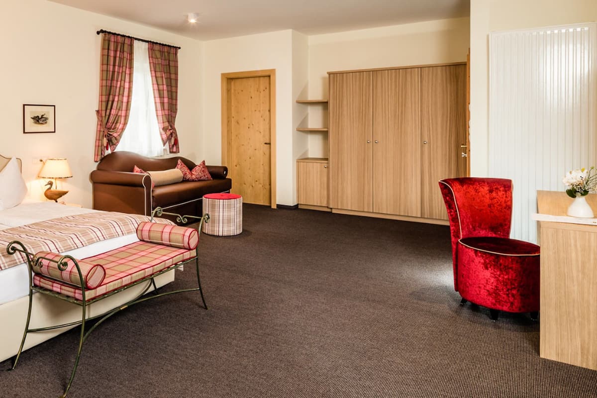Ein Hotelzimmer mit Bett, Nachttischen, Schreibtisch, Stuhl, Kleiderschrank und einem Fenster mit Vorhängen.