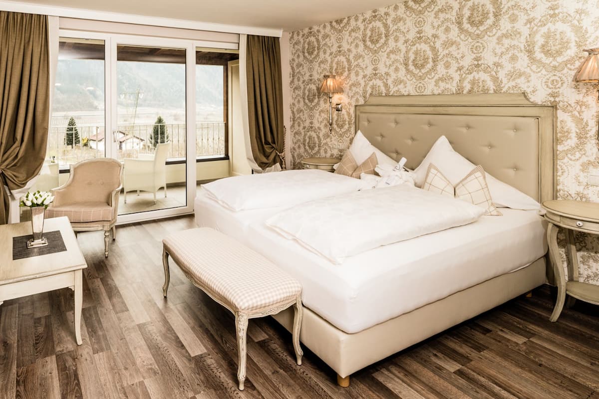 Ein Hotelzimmer mit einem großen Bett, einer Couch, einem kleinen Tisch, einer Bank und Blick auf die Berge durch das Fenster.