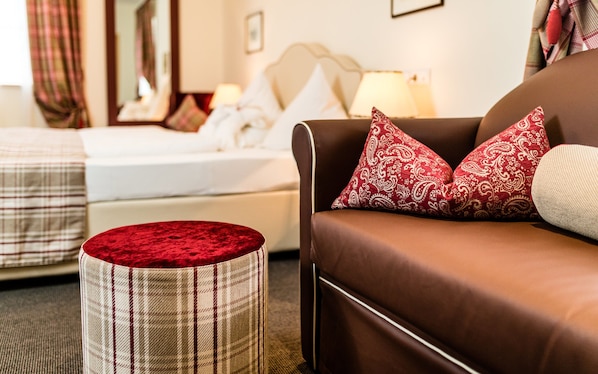 Una habitación de hotel con una cama, un sofá marrón con cojines estampados y un reposapiés de cuadros.