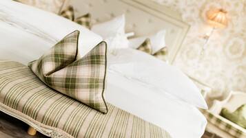 Cama com almofadas xadrez e uma almofada listrada, cabeceira de madeira e parede com padrão floral.