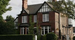 Un edificio de estilo Tudor tradicional con una chimenea destacada, múltiples ventanas y un seto bien cuidado al frente.