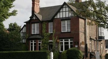 Un edificio de estilo Tudor tradicional con una chimenea destacada, múltiples ventanas y un seto bien cuidado al frente.
