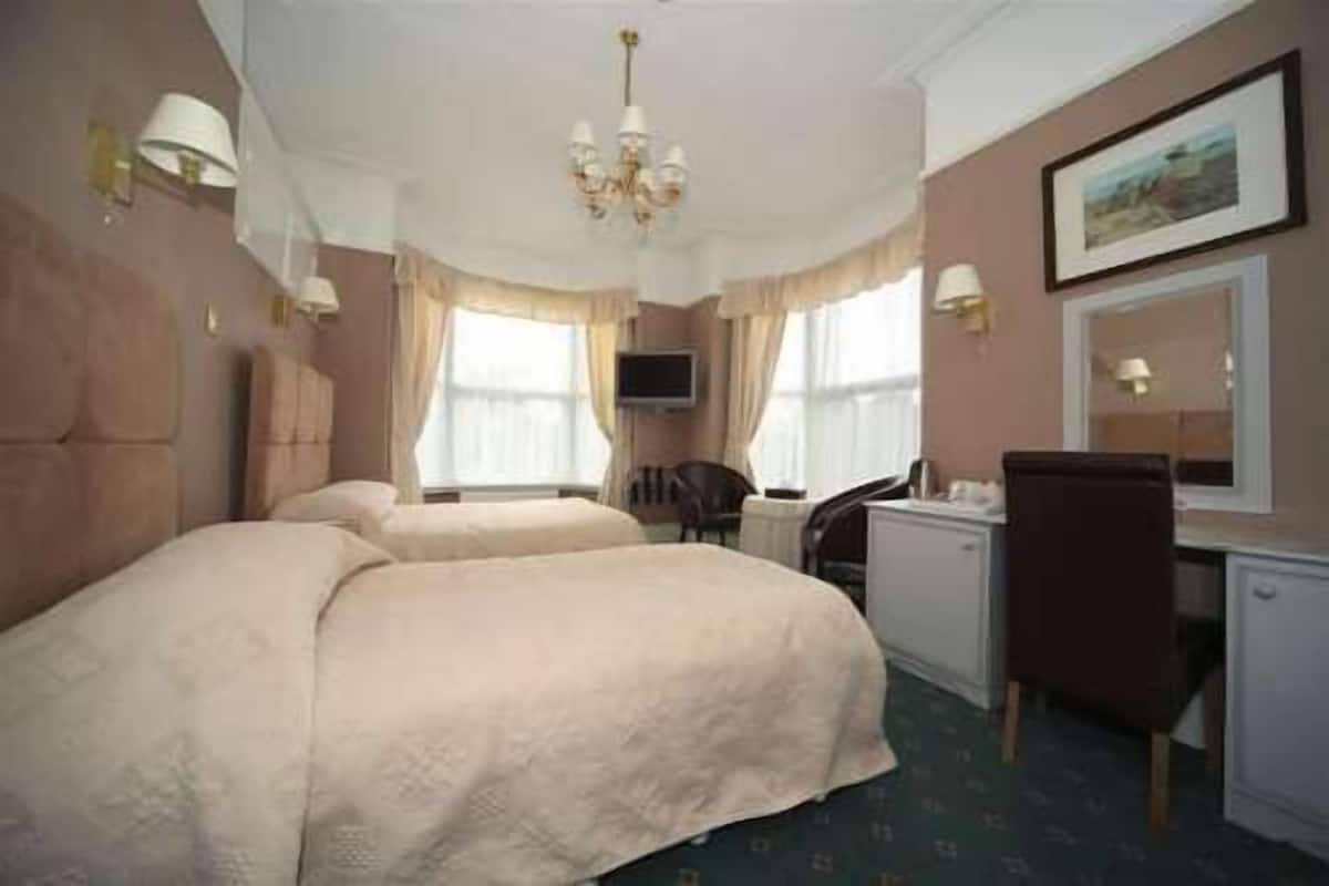 A hotel room with two beds, a desk, a chair, a TV, and a chandelier.
