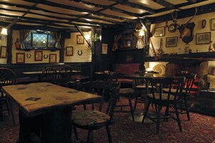 Un pub tradicional con vigas de madera a la vista, decoración rústica y diversas opciones de asientos, incluyendo mesas y sillas.