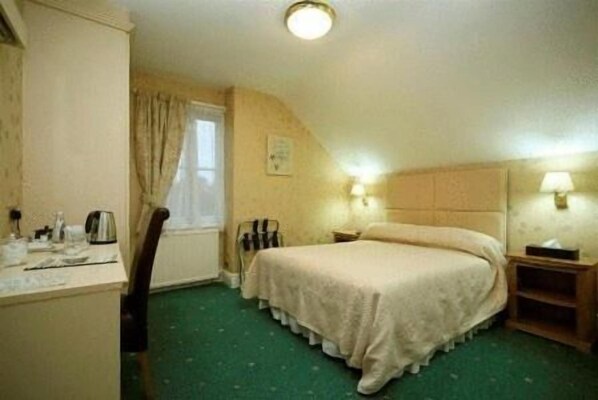 Habitación de hotel con una cama individual, un escritorio con silla, una ventana con cortinas y una mesita de noche con lámpara.