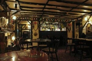 Un área de bar tenuemente iluminada, con vigas de madera en el techo, mesas y sillas dispuestas para los clientes.