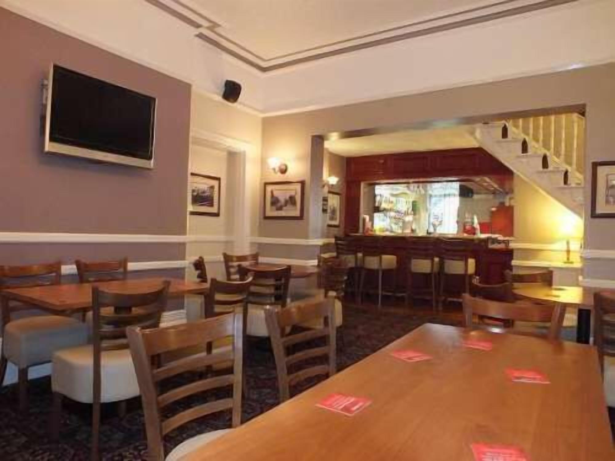 Un comedor de hotel con varias mesas y sillas de madera, una zona de bar con taburetes y cuadros en las paredes.