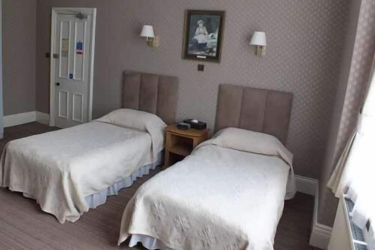 A hotel room with two single beds, a small bedside table, a door, and a wall-mounted picture.