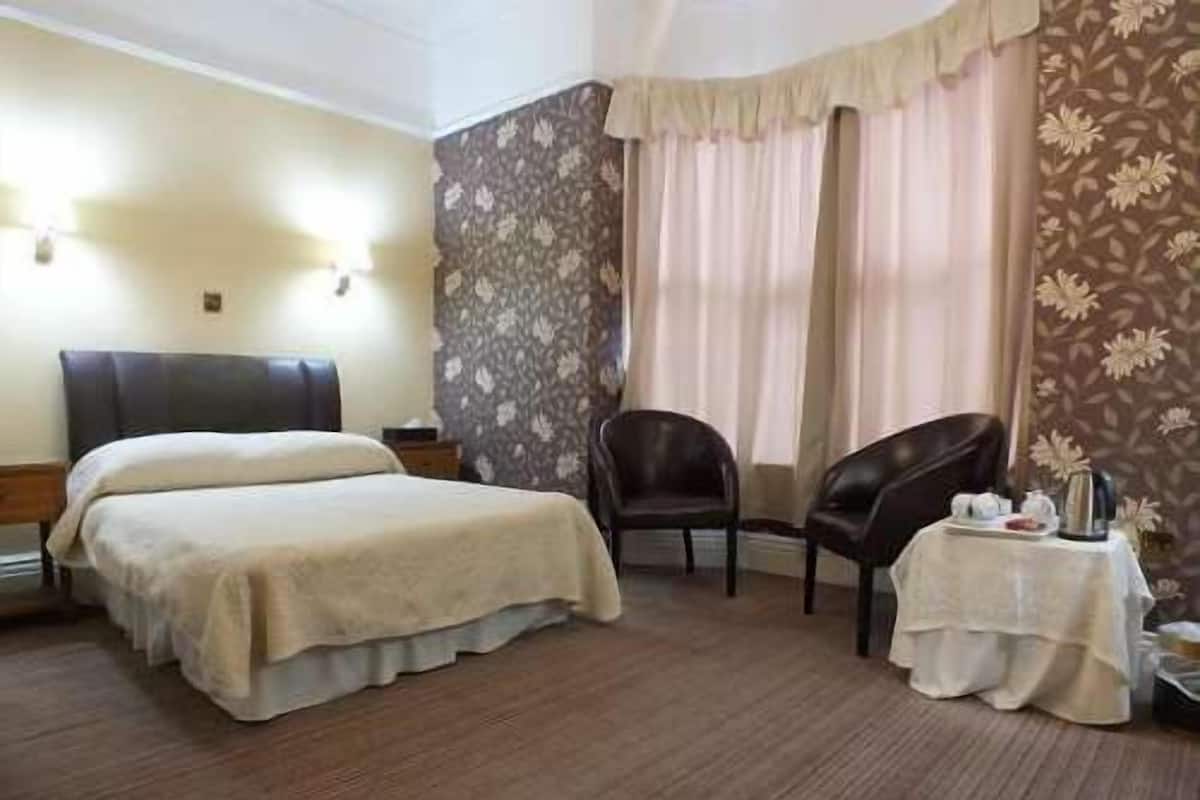 A hotel room with a bed, a chair, a small table with a tray, and a window with curtains.