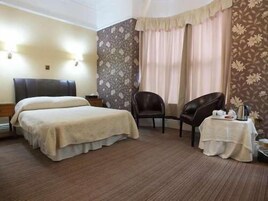 Habitación de hotel con cama, una silla, una mesita con bandeja y ventana con cortinas.