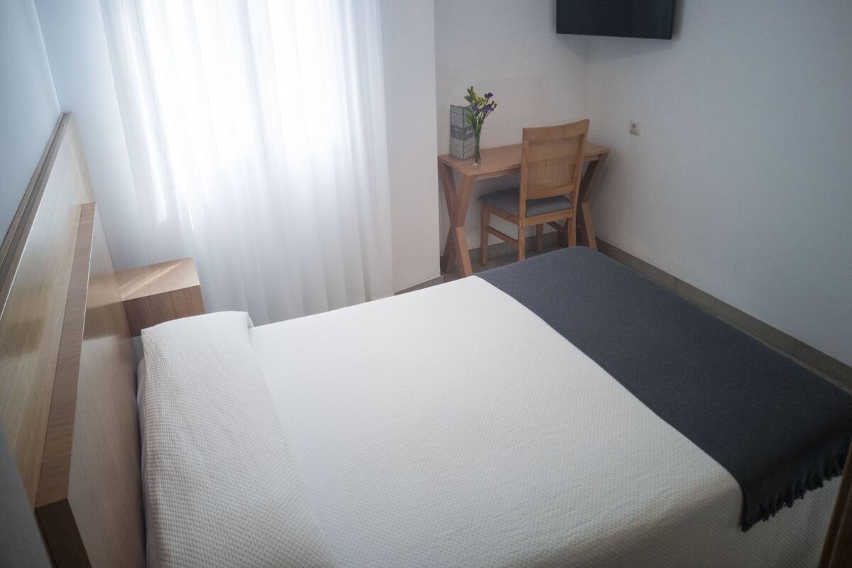 A hotel room with a bed, a desk, a chair, and a TV on the wall.