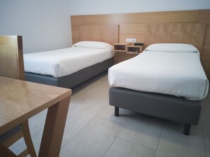 A hotel room with two single beds, a wooden headboard, a small bedside table with a lamp, and a wooden desk. - Abadi (Córdoba)