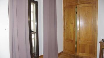 Una habitación con un armario de madera, una puerta con panel de vidrio y una cortina.