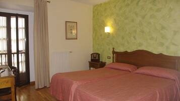 A room with a bed, a desk, a chair, a radiator, a picture on the wall, and a window with curtains.