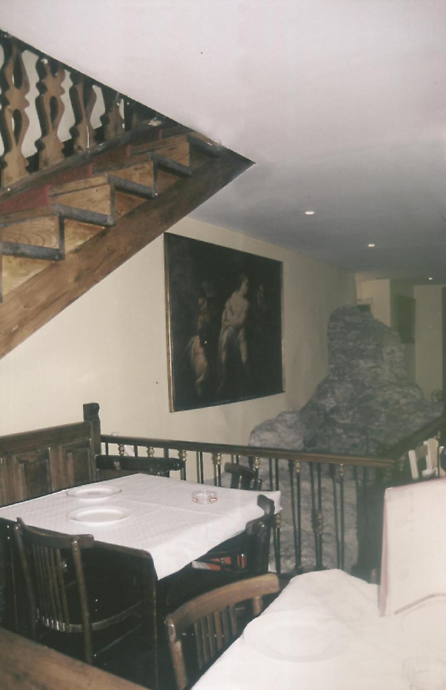 Un comedor con una mesa, sillas, una escalera y un cuadro grande en la pared.