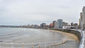 A coastal cityscape with a curved promenade, a sandy beach, and a stone wall with a white railing. - Hotel La Casona de Jovellanos (Gijon)