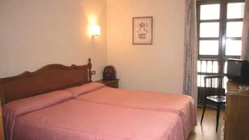 Un dormitorio con una cama doble, una mesita de noche con lámpara, un cuadro en la pared y una ventana con cortinas.