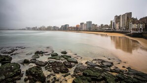 Un paisaje urbano costero con una playa de arena y un primer plano rocoso.