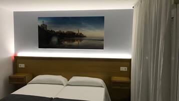 A hotel room with a bed, two bedside tables, a nightstand, a painting of a cityscape, and a curtain.