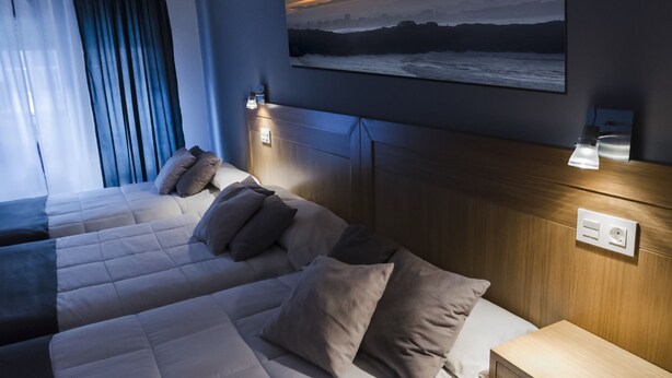 Una habitación de hotel con dos camas, un cuadro grande de una puesta de sol y lámparas de noche.