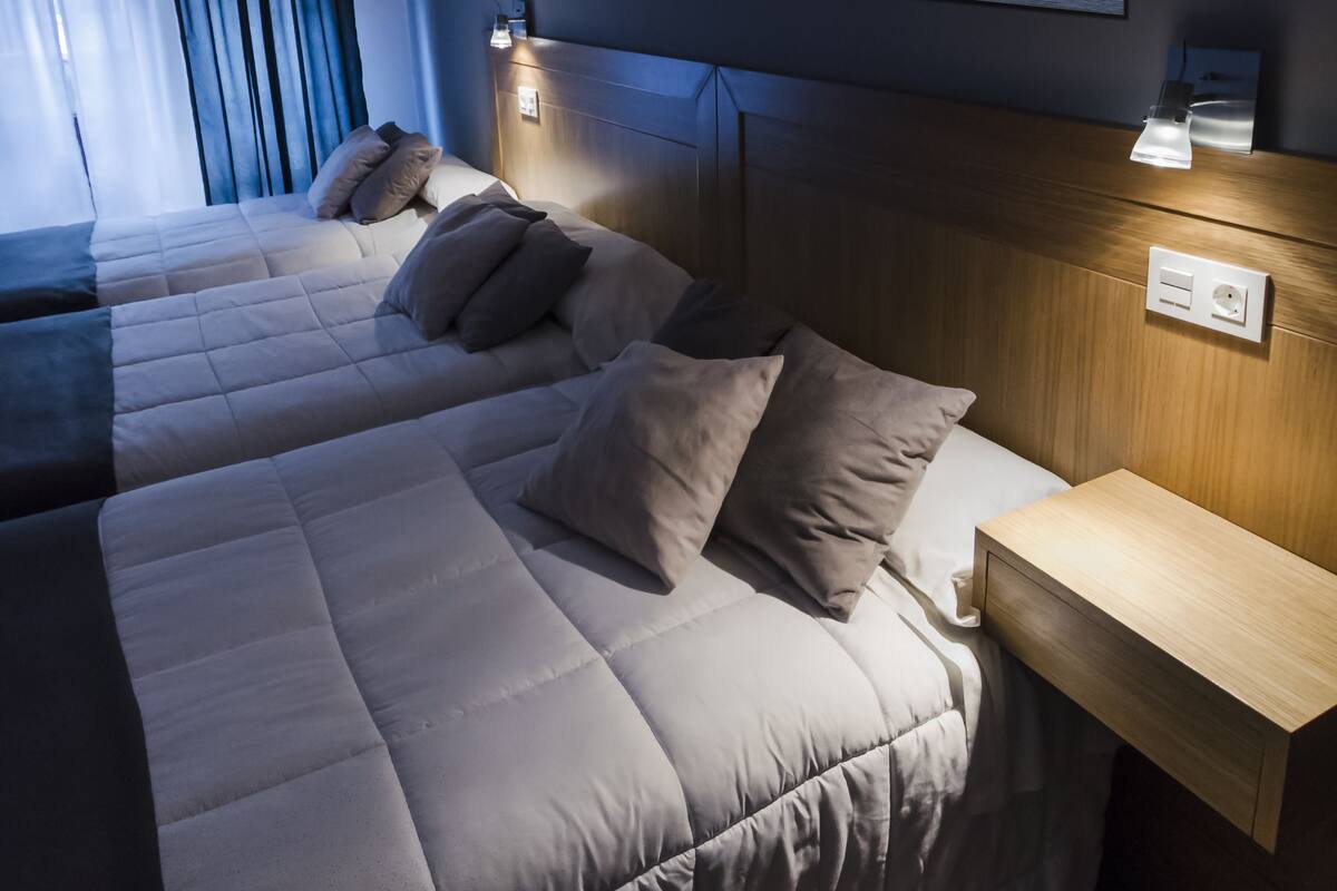 A hotel room with two beds, a large painting of a sunset, and bedside lamps.