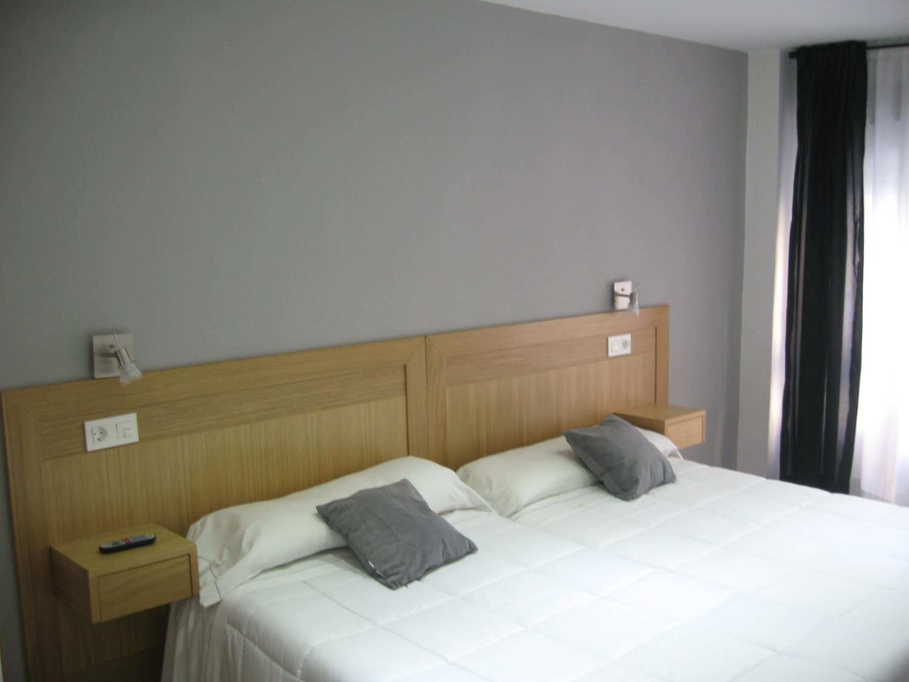 Una habitación de hotel con una cama grande, dos mesitas de noche y un ventanal con cortinas.
