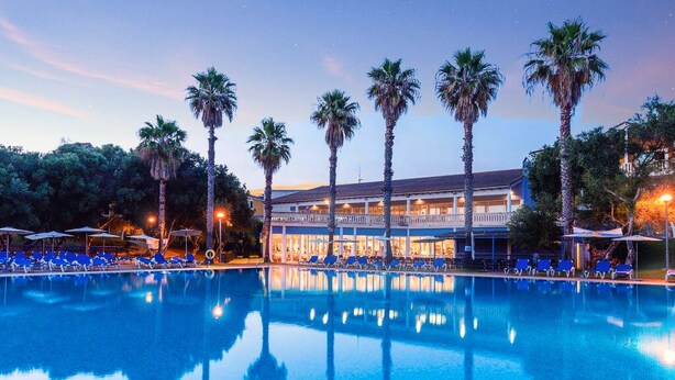 A swimming pool with palm trees and a building in the background. - Vibra Blanc Palace Aparthotel (Ciutadella de Menorca)